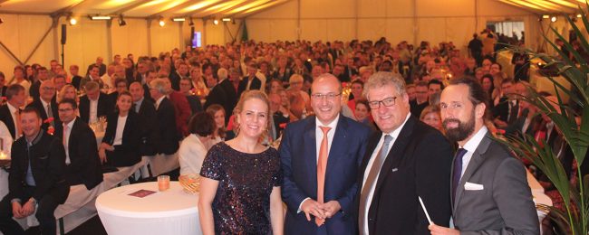 Arnulf und Olaf Piepenbrock mit Thomas Cord mit zwei weiteren Personen bei der Jubiläumsfeier von LoeschPack mit Gästen im Hintergrund.