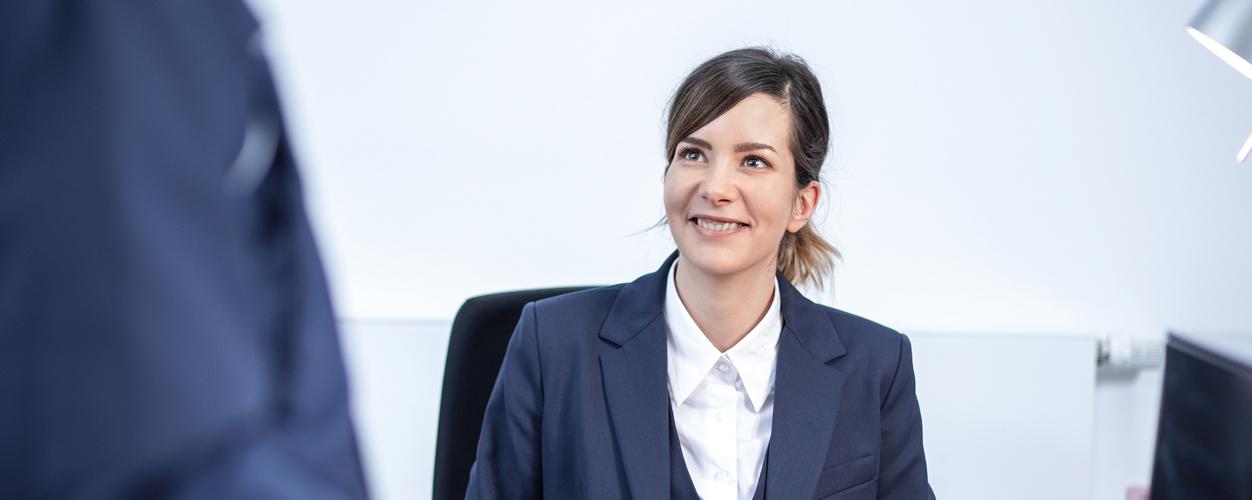 Dame sitzt am Empfang und schaut zu Besucher hoch