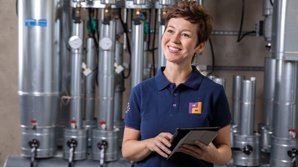 Piepenbrock Mitarbeiterin in Arbeitskleidung mit Tablet vor technischer Anlage