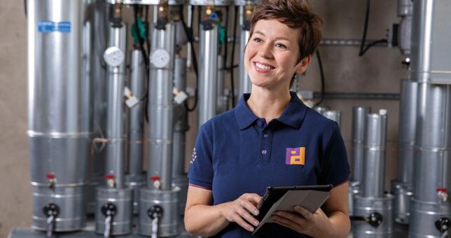 Piepenbrock Mitarbeiterin in Arbeitskleidung mit Tablet vor technischer Anlage