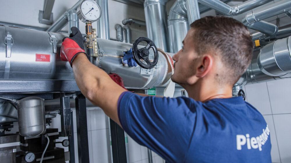 Piepenbrock Mitarbeiter mit blauem T-Shirt und roten Arbeitshandschuhen bei der Arbeit als Objektmanager mit unterschiedlichen Rohren