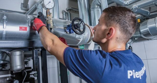 Piepenbrock Mitarbeiter mit blauem T-Shirt und roten Arbeitshandschuhen bei der Arbeit als Objektmanager mit unterschiedlichen Rohren