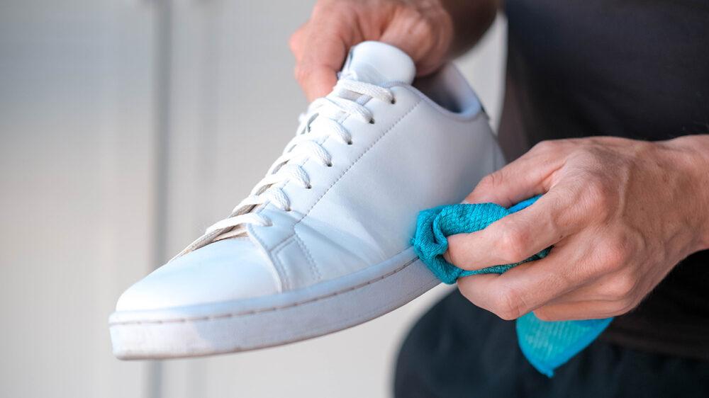Weißer Sneaker wird mit einem blauen Tuch gereinigt.