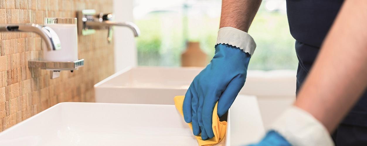 Person mit blauen Hygiene-Handschuhen bei der Sanitärreinigung eines Waschbeckens