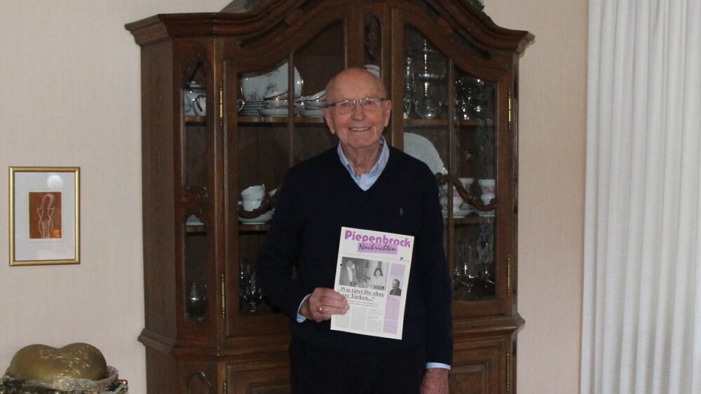 Ehemaliger Piepenbrock Niederlassungsleiter Georg Werning mit alter Ausgabe der Piepenbrock Nachrichten im Wohnzimmer vor einem Schrank.