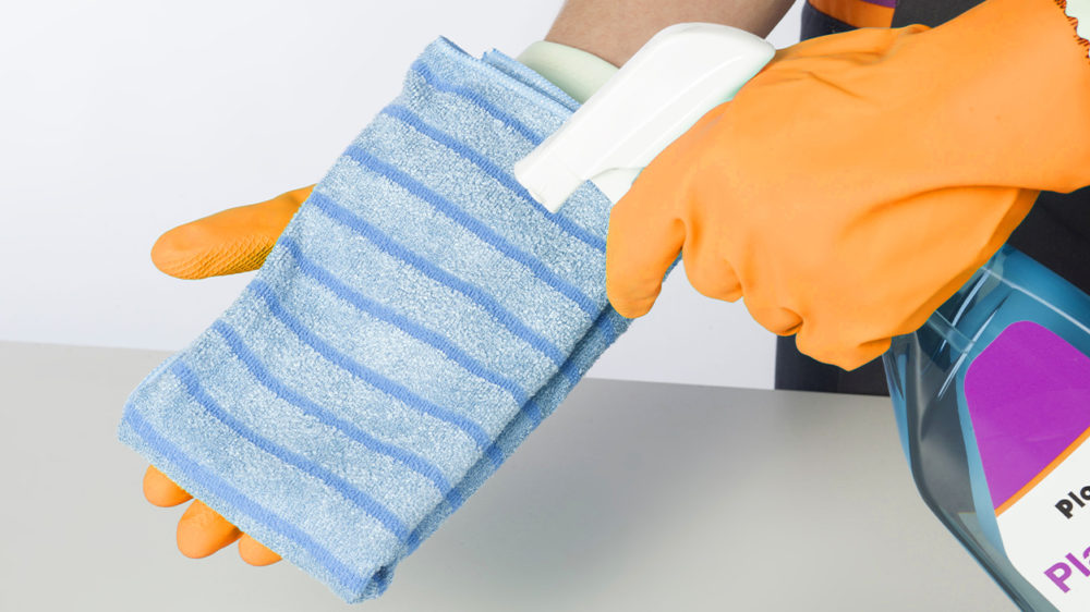 Nahaufnahme Blaues Reinigungstuch, auf das Reinigungsmittel aus Sprühflasche aufgesprüht wird