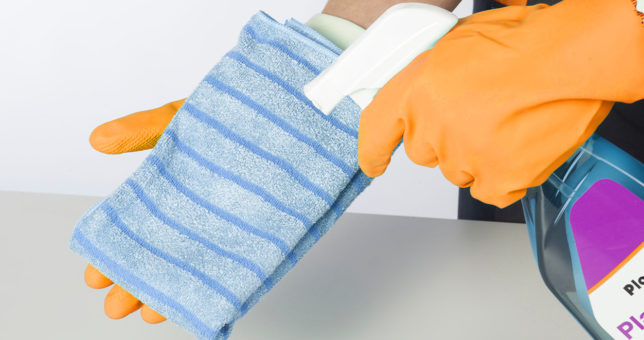 Nahaufnahme Blaues Reinigungstuch, auf das Reinigungsmittel aus Sprühflasche aufgesprüht wird