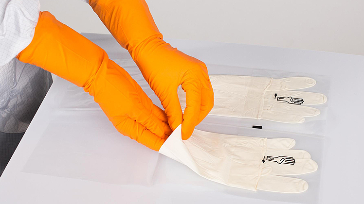 Hände mit orangenen Gummihandschuhen, die nach einem weißen Handschuh greift.