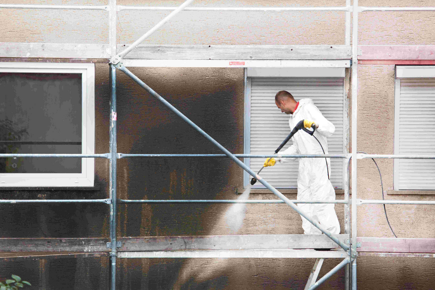 Piepenbrock Mitarbeiter reinigt verschmutzte Fassade auf Gerüst mit Hochdruckreiniger und entfernt Rußablagerungen