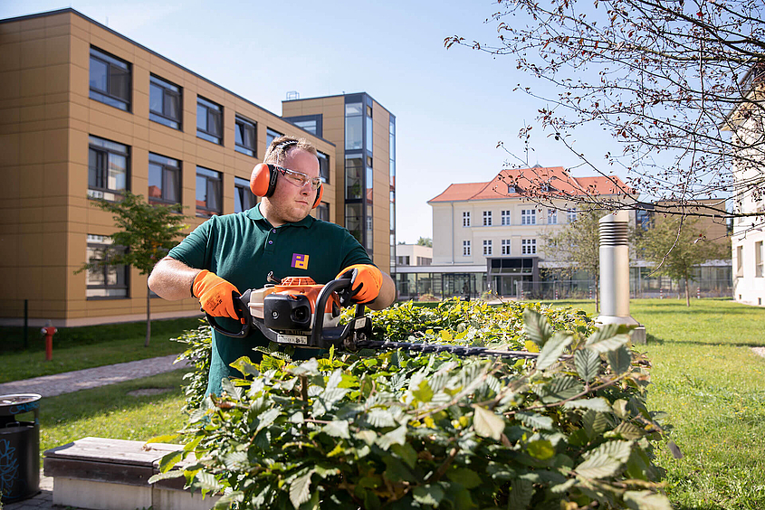 Mitarbeiter des Infrastrukturellen Facility Management führt Grünpflege durch