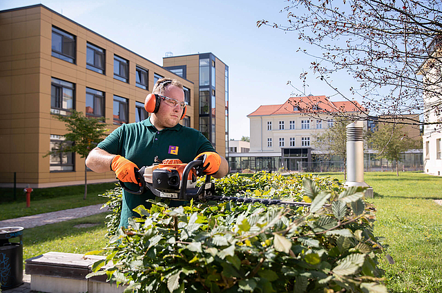 Mitarbeiter des Infrastrukturellen Facility Management führt Grünpflege durch
