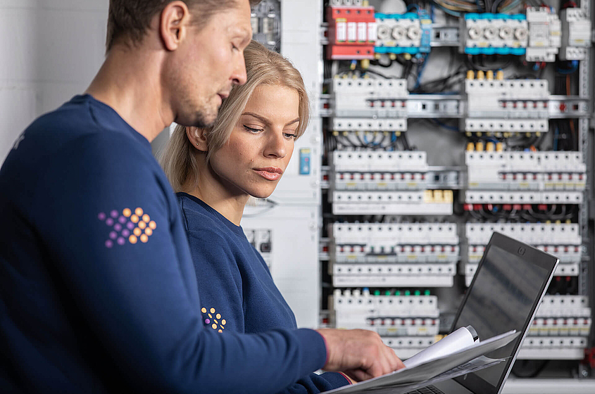Mitarbeiter des Prüfservice stimmen sich vor einem Schaltkasten ab